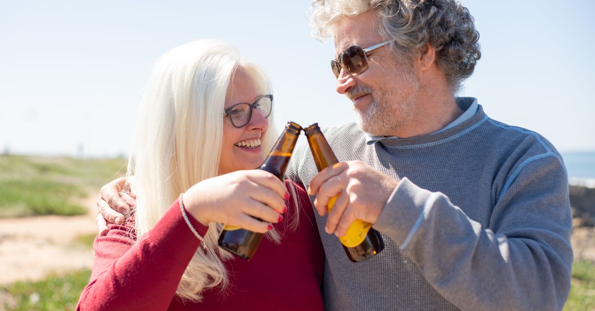 Senior couple enjoying a sunny day outdoors, toasting with beer bottles, embodying joy and companionship.