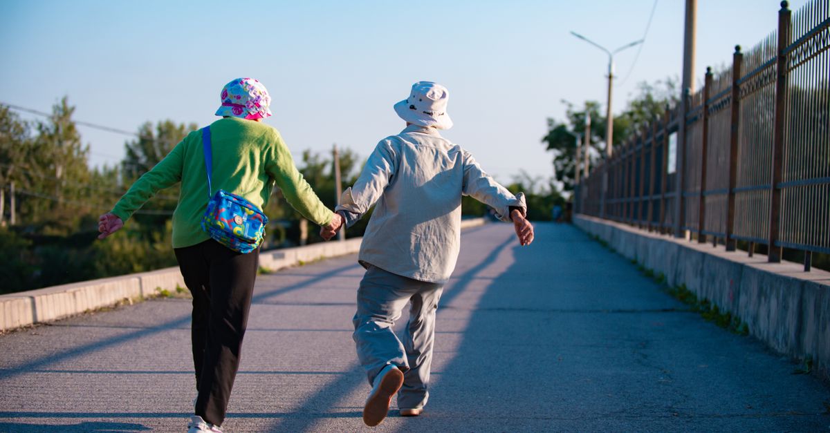 Elderly couple in colorful attire walking hand in hand on a sunny day.