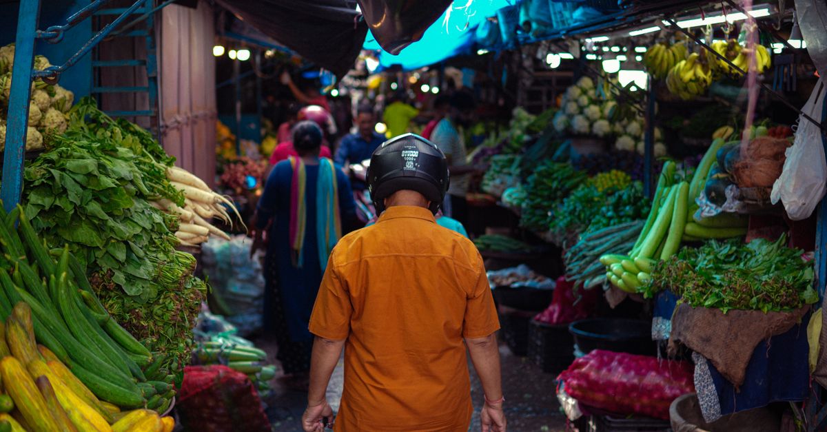 Crowded market with diverse vegetables and people shopping. Vibrant street life captured.