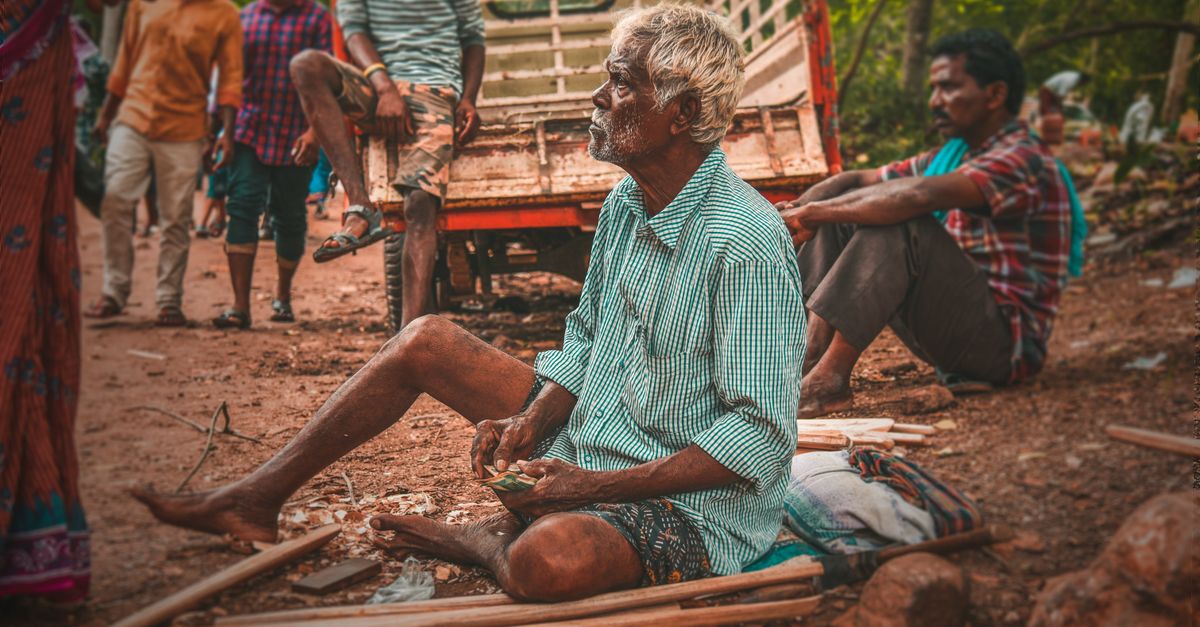 Elderly man sitting and selling crafts on a bustling street in Eluru, India.