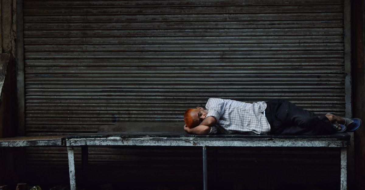 A man sleeps on a metal bench in an urban setting, illustrating homelessness.