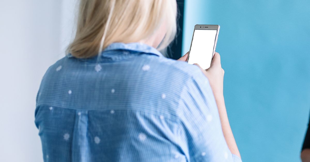 Blonde woman using a smartphone indoors. Back view showing leisure time.