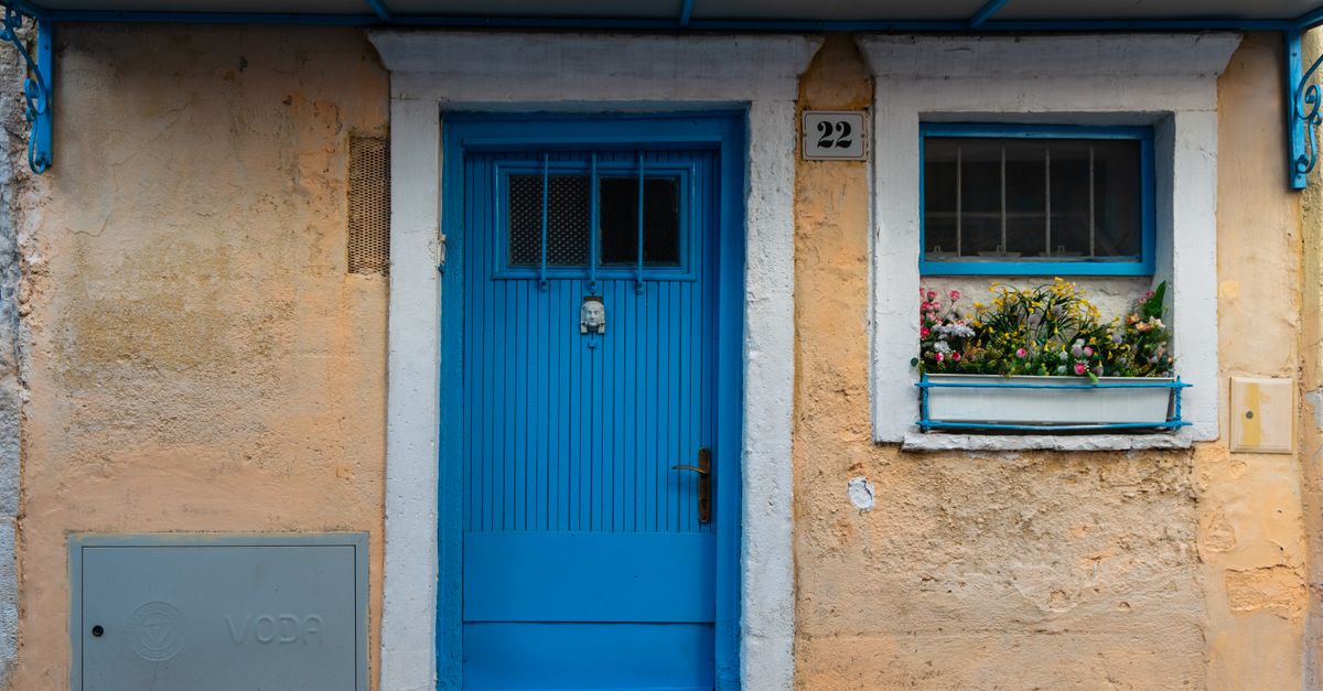 A vibrant blue door with floral window decor on a rustic urban facade, perfect for architecture enthusiasts.