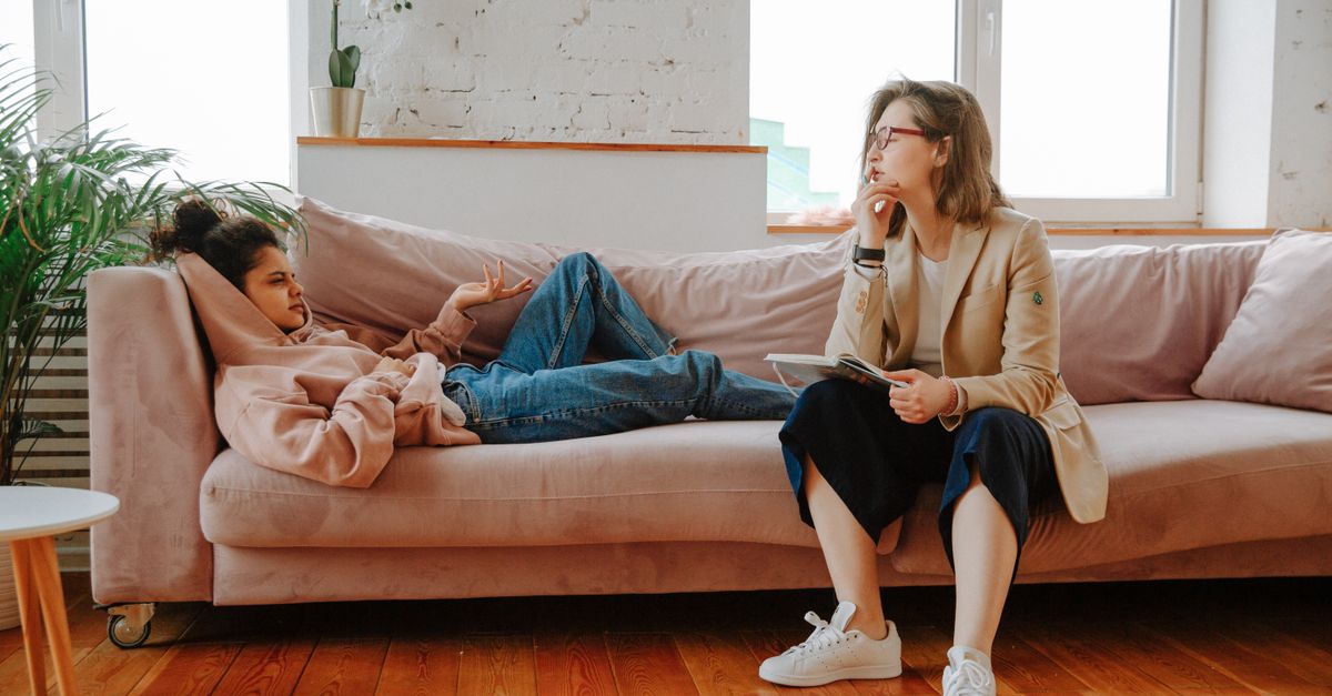 A young woman in a hoodie engages with a therapist during a counseling session indoors.