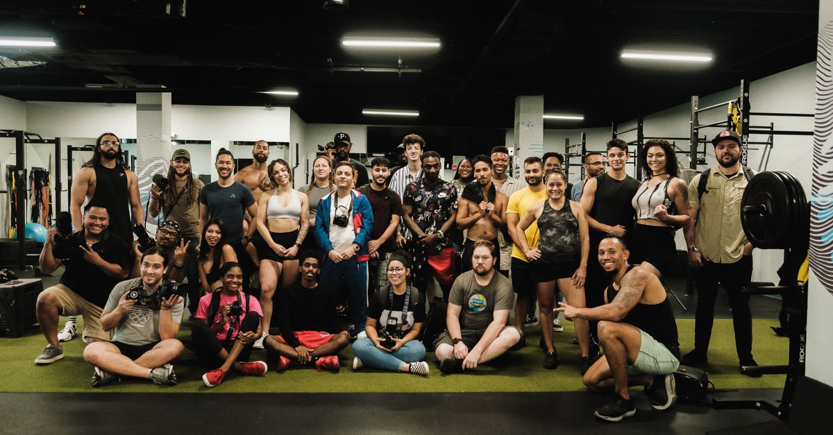 A large group of diverse adults smiling and posing together in a gym setting.