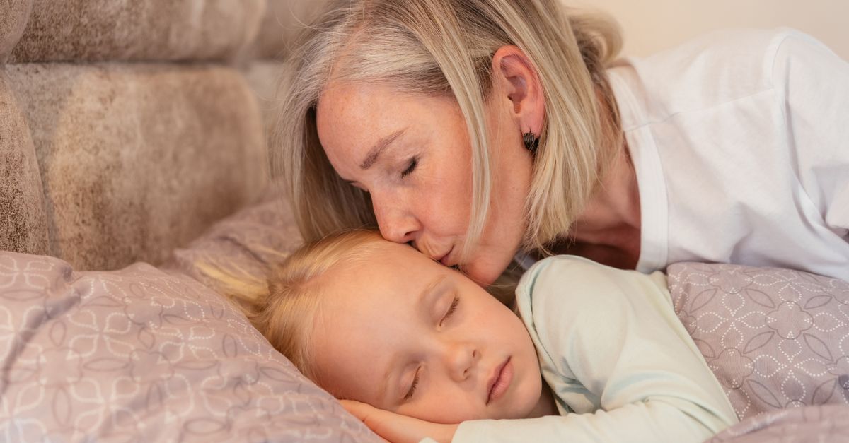 A loving grandmother kisses her sleeping grandchild in a cozy bedroom setting.