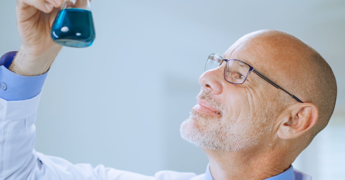 Male scientist examining blue liquid in a lab flask. Science and research concept.