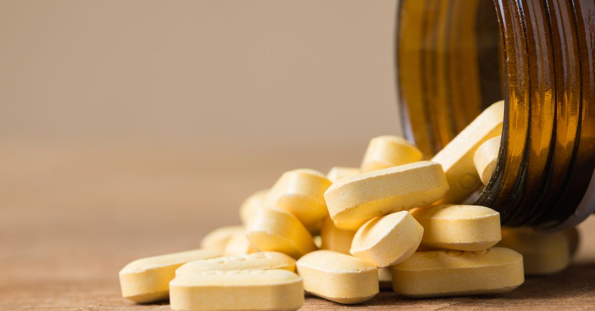 A close-up image of vitamin tablets spilling out of a transparent brown bottle on a wooden surface.