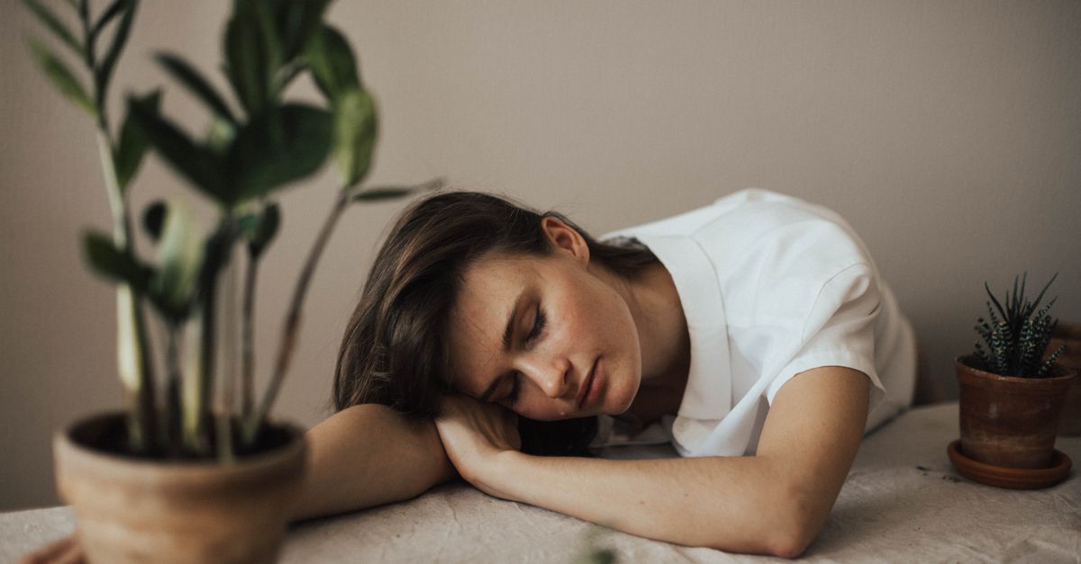 A woman peacefully resting her head on a table surrounded by indoor plants.