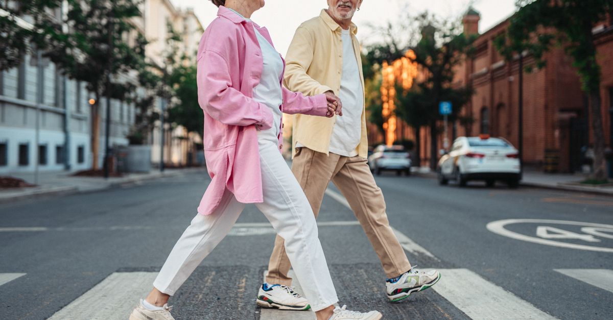 Happy senior couple holding hands and walking across a pedestrian crossing in an urban street.