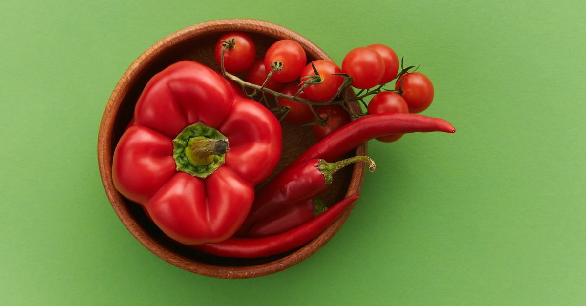 Fresh red peppers and cherry tomatoes in a wooden bowl on a vibrant green background.