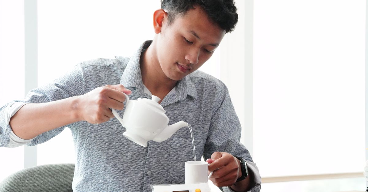 Adult male pouring tea into a cup in modern indoor environment, emphasizing relaxation and hospitality.