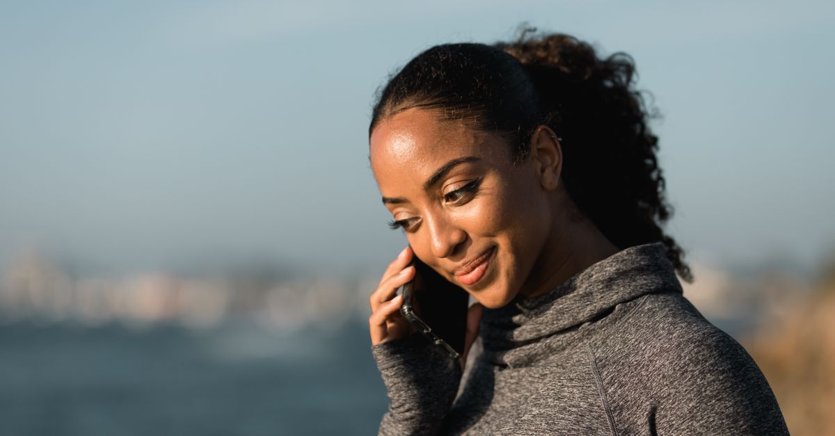 A woman smiling during a phone call, with a serene ocean background.