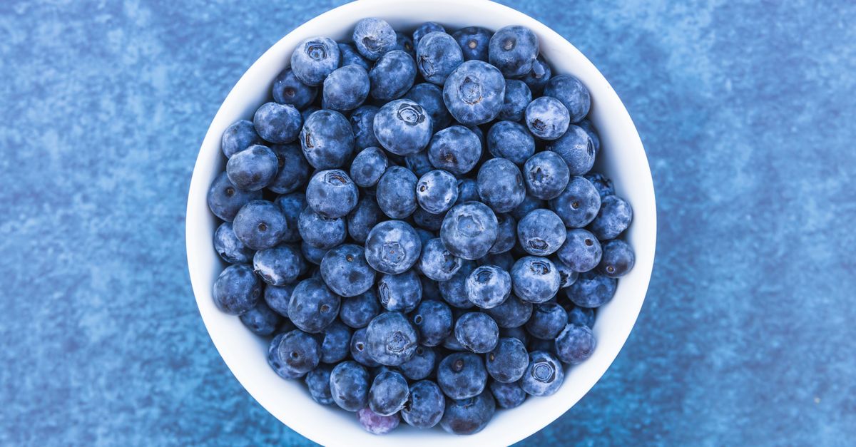 Top view of fresh blueberries in a white bowl on a textured blue background.