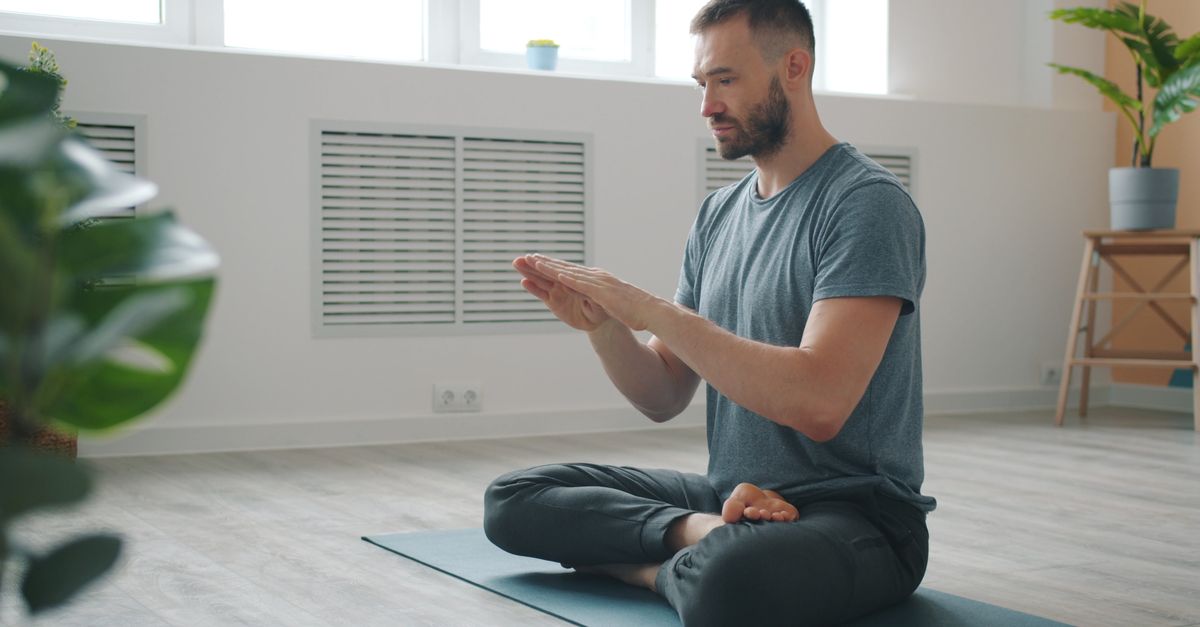 Adult man meditating on a yoga mat in bright indoor space, focusing on self-care and mindfulness.