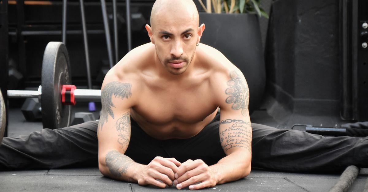 Bald man with tattoos stretching in gym, showcasing strength and flexibility.