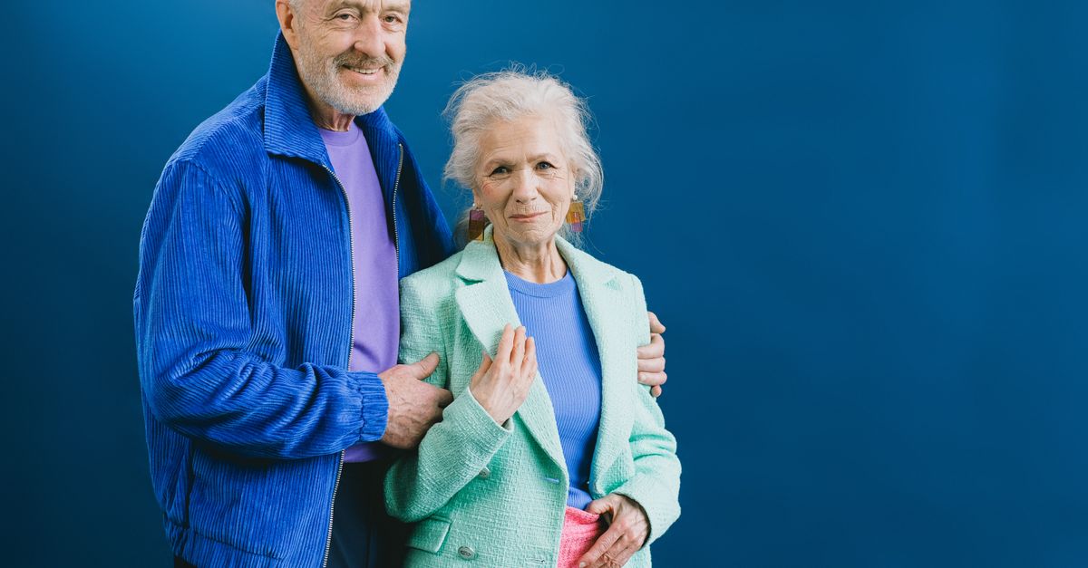 Senior couple posing confidently in stylish outfits against a blue backdrop.