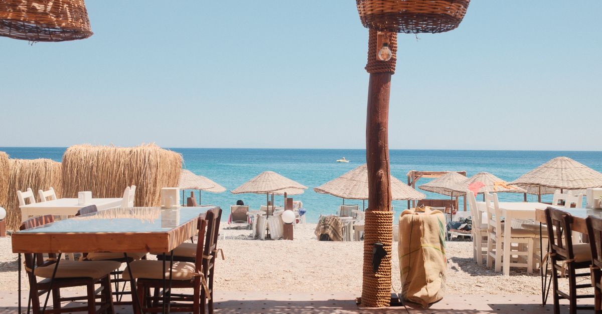 Outdoor dining by the beach with straw umbrellas and blue sea view.