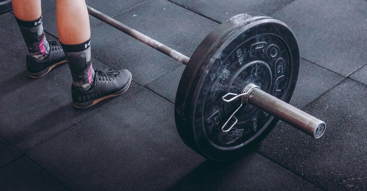 Close-up of an athlete's legs beside a barbell, ready for weightlifting in a gym.