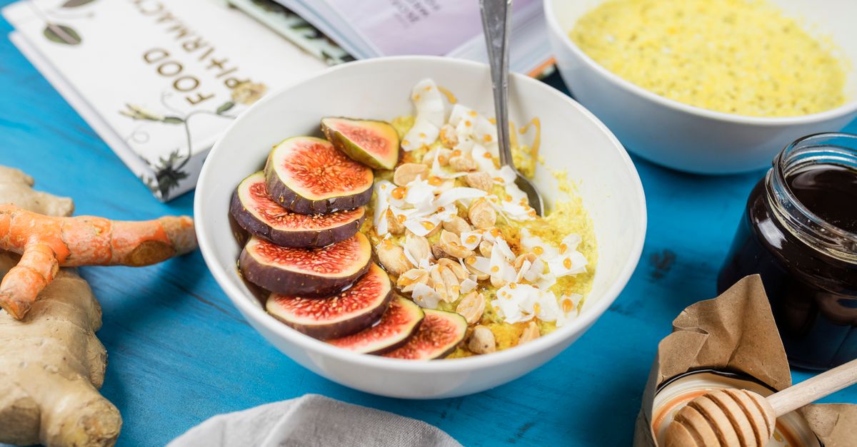 Healthy breakfast bowl with figs, nuts, and turmeric on a blue table with ginger and honey.