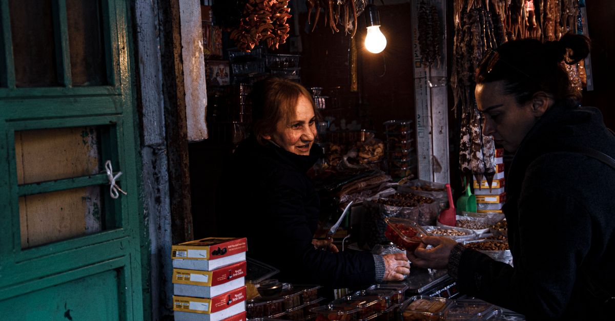 A vendor engaging with a customer at a cozy, dimly-lit market stall displaying various food items.
