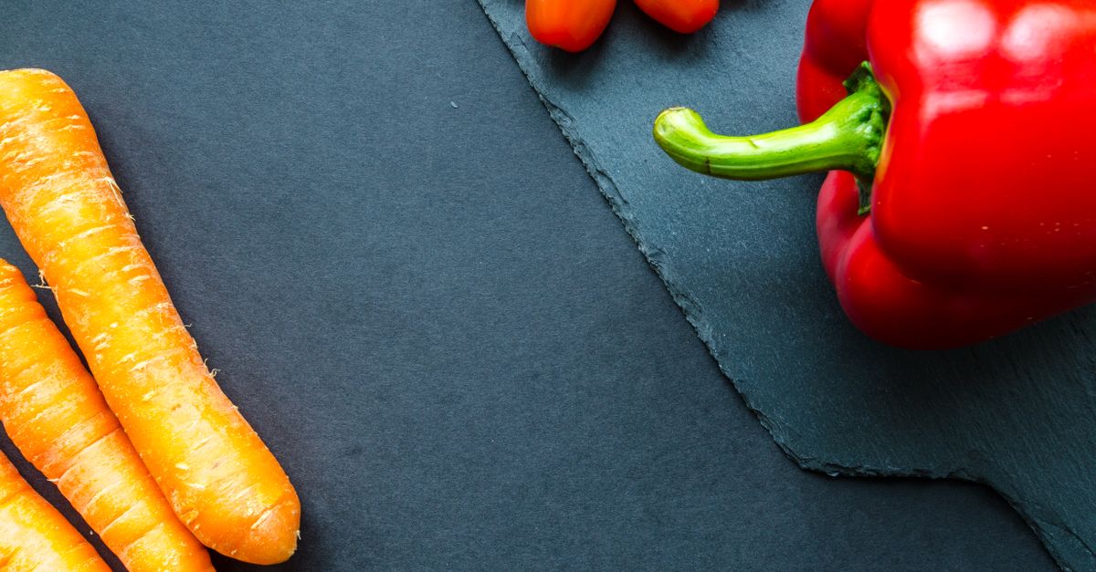 Colorful arrangement of fresh carrots, tomatoes, and bell pepper on a slate surface.