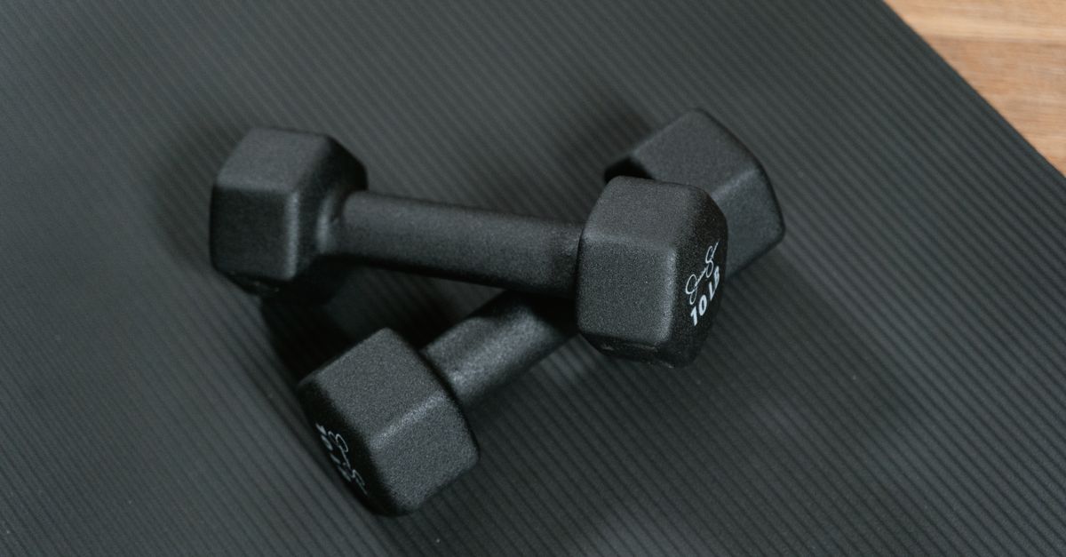 Black dumbbells placed on a yoga mat, perfect for home workouts and strength training.