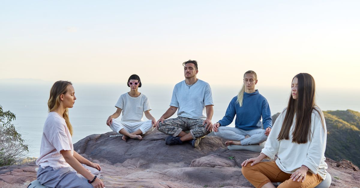 Five adults meditating outdoors on a mountain top during sunrise, promoting relaxation and mindfulness.