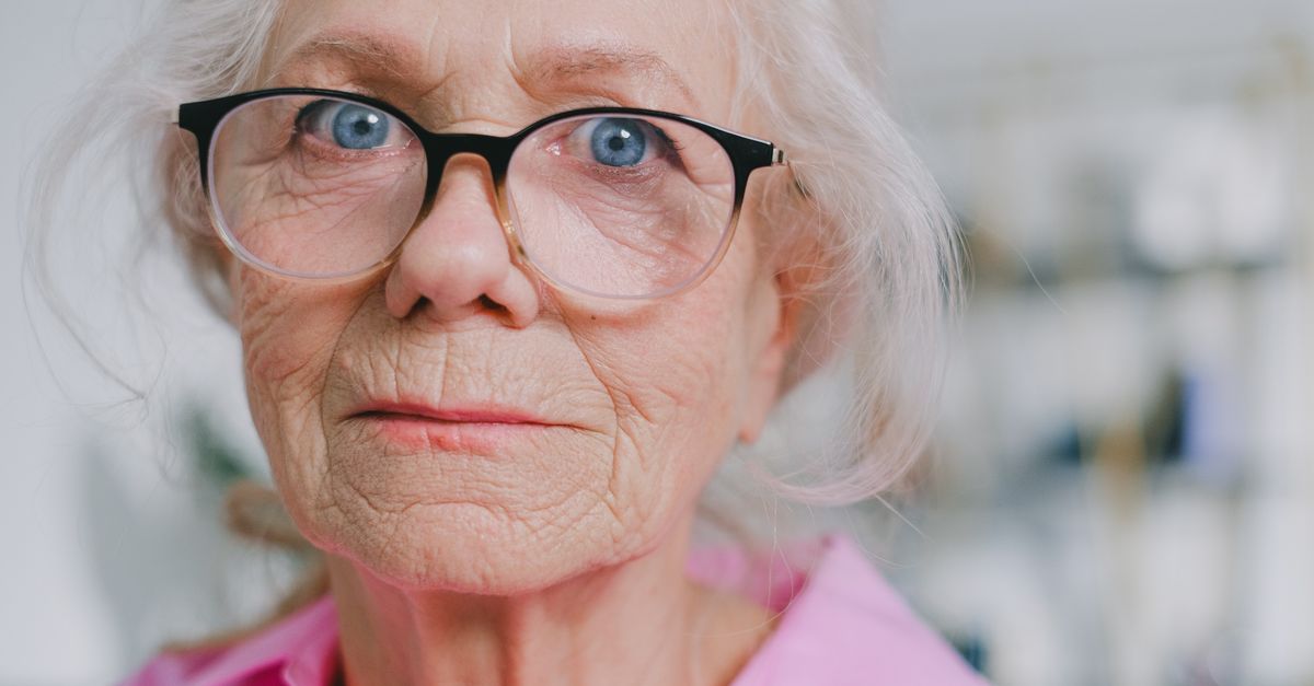 Elderly woman wearing glasses, looking thoughtful in a close-up portrait.
