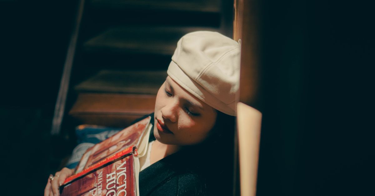 Woman with a beret holding Victor Hugo books, sitting on stairs.