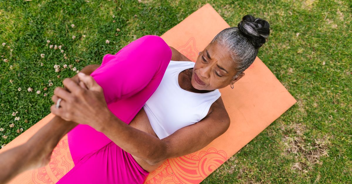 Elderly woman performing yoga stretch on grass for wellness.