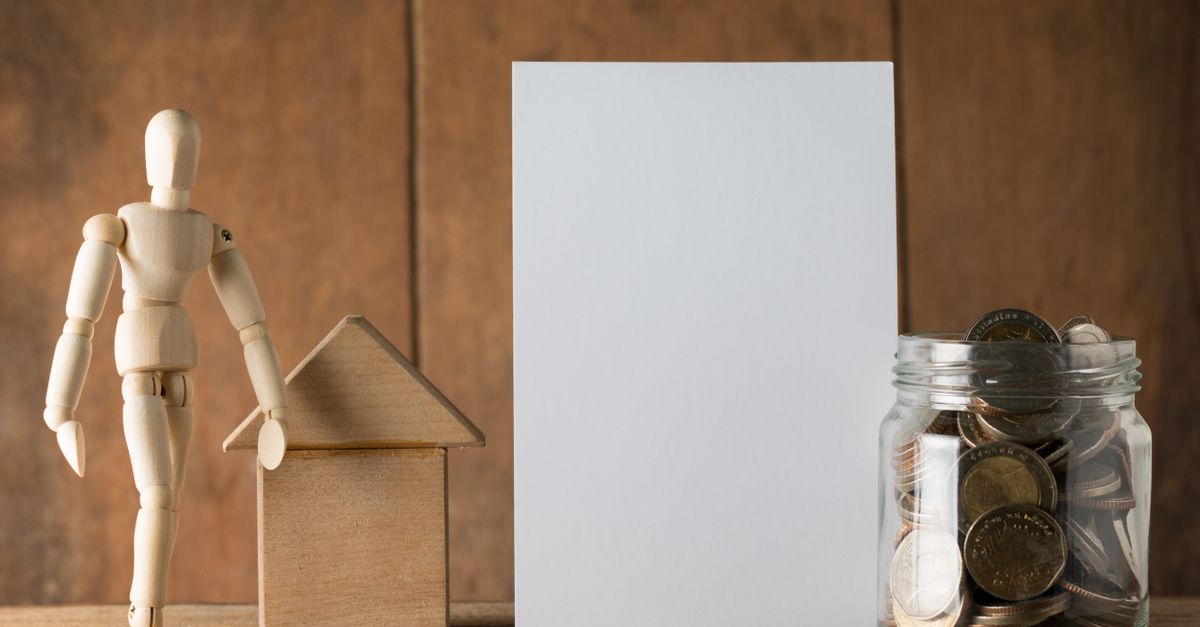 Wooden figure with jar of coins and blank card for financial planning or savings concept.