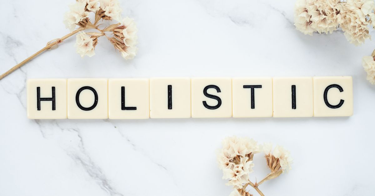 Flat lay of 'holistic' spelled in letter tiles on marble with dried flowers.
