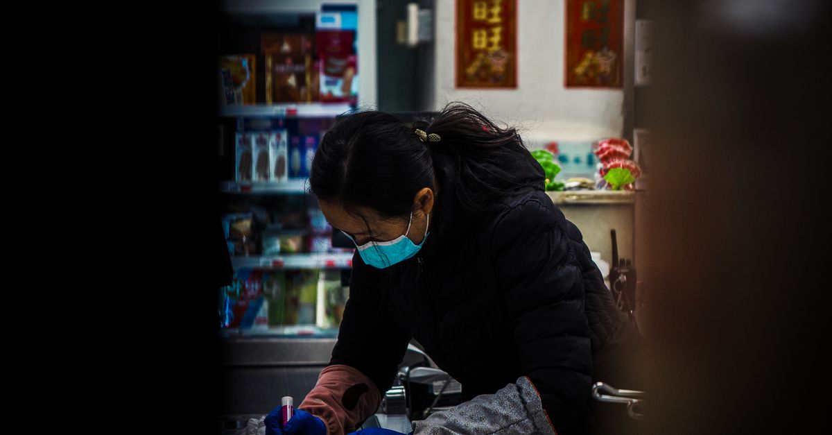 An Asian woman wearing a mask focuses on her work inside a store.