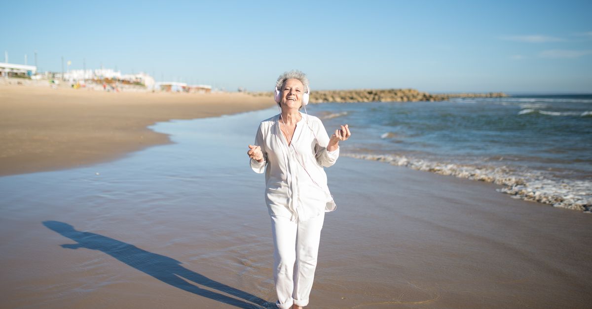 Happy senior woman in white enjoys music on a sunny beach in Portugal.