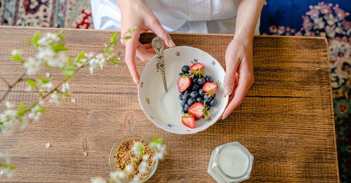 A top view of a person preparing a healthy breakfast with fresh berries, milk, and granola on a wooden table.