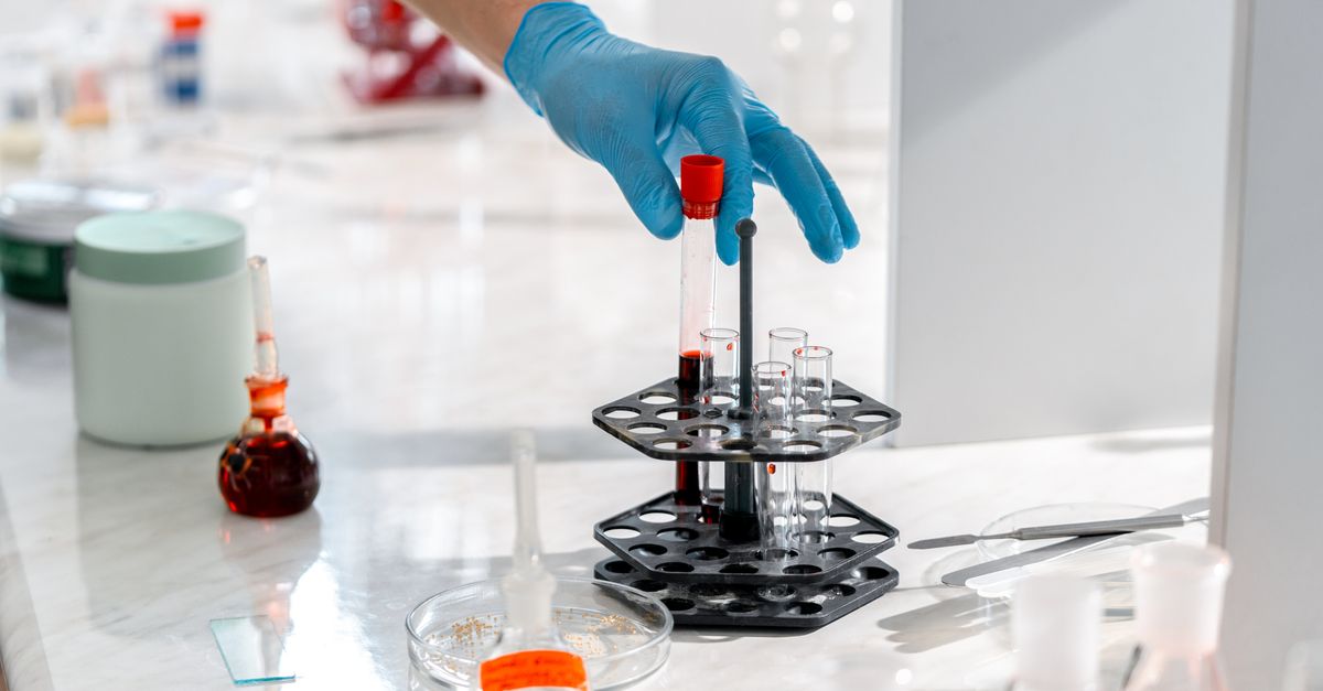 Close-up of a gloved hand handling test tubes in a bright laboratory setting.