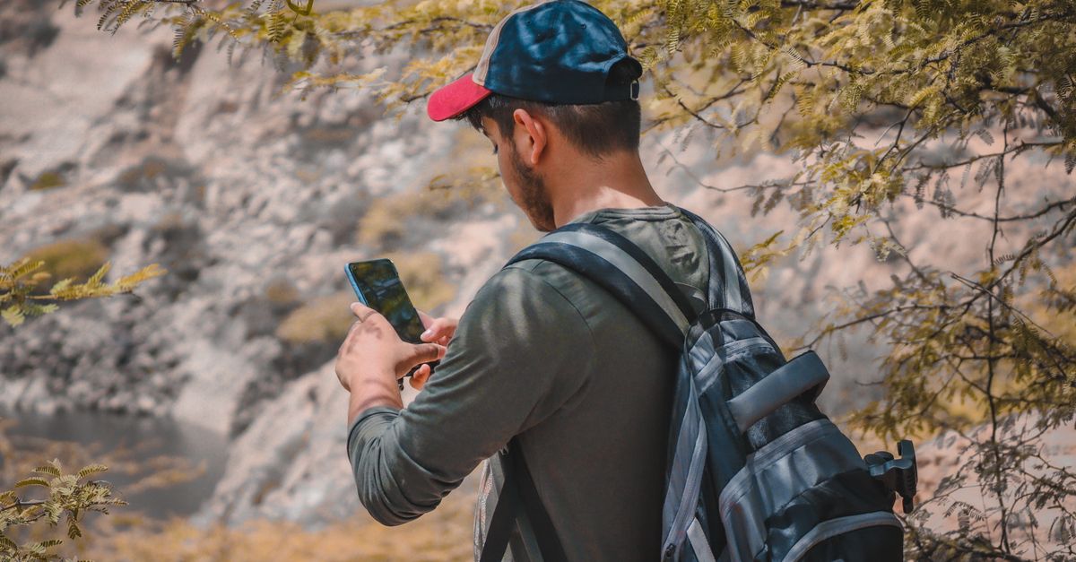 A young man hiking outdoors, using a smartphone in the scenic landscape of New Delhi, India.