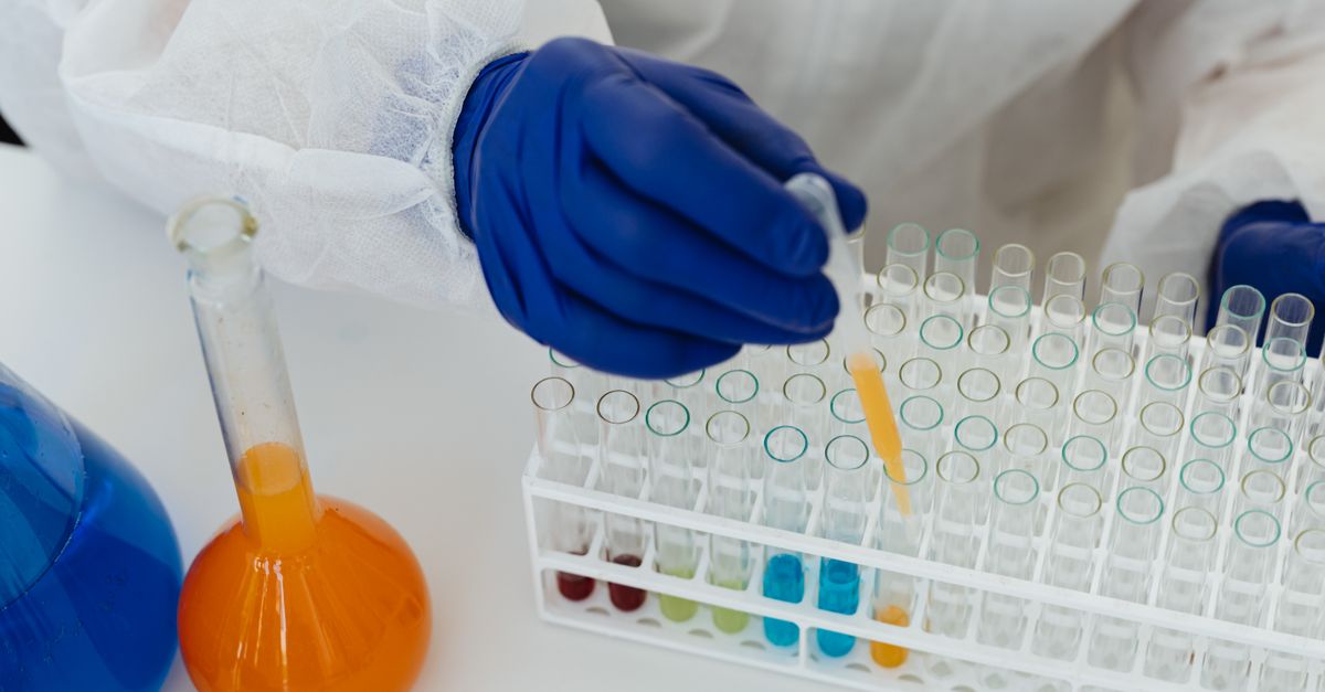A scientist in blue gloves uses a pipette to handle colored liquids in a laboratory setting.