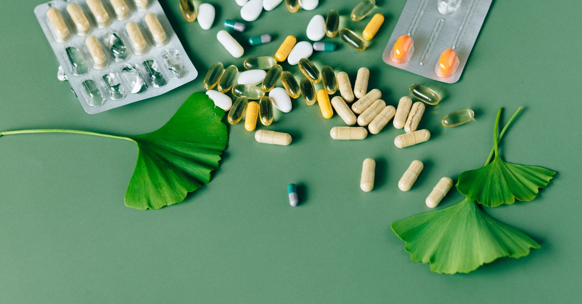 A variety of natural supplements and pills displayed on a green background with Ginkgo biloba leaves.