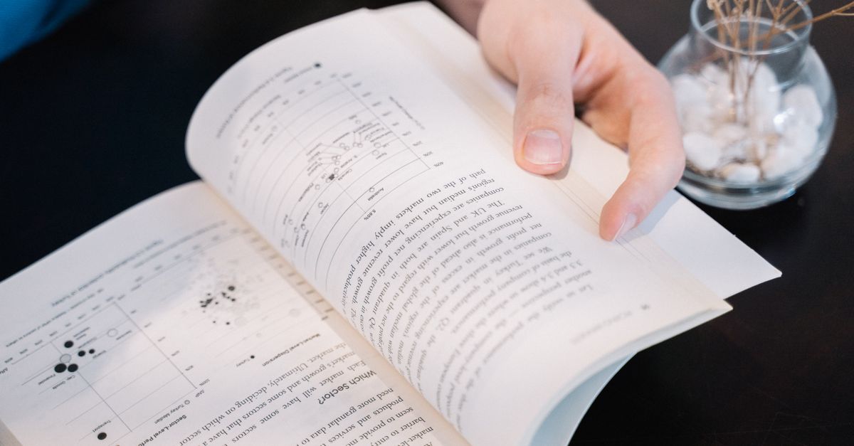 Close-up of a hand turning pages in a book with data charts and text.