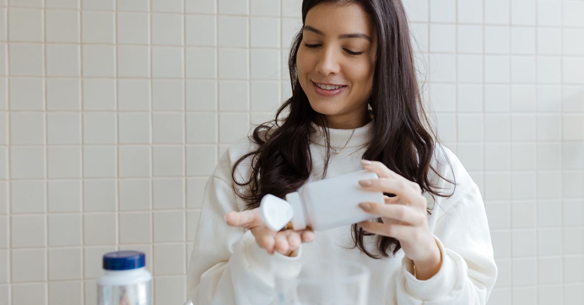 A woman smiles as she pours pills from a bottle into her hand, capturing a healthcare moment.