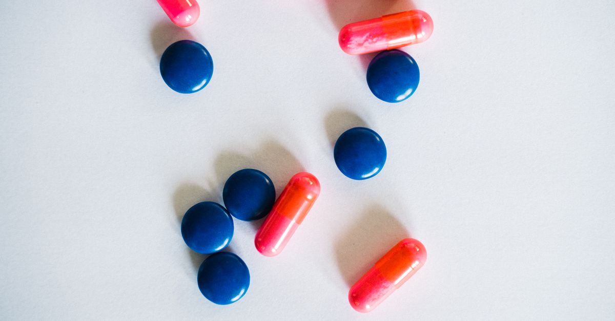 A collection of pink capsules and blue pills scattered on a white background.