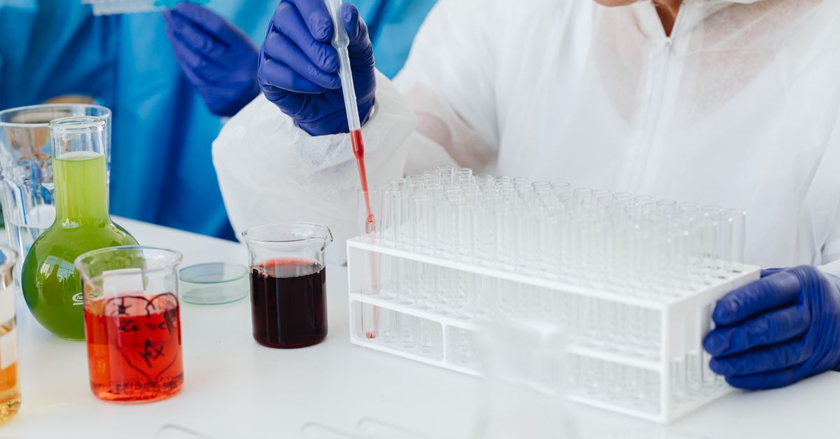 Female scientist in lab coat using pipette on test tubes, focusing on colorful chemical analysis.