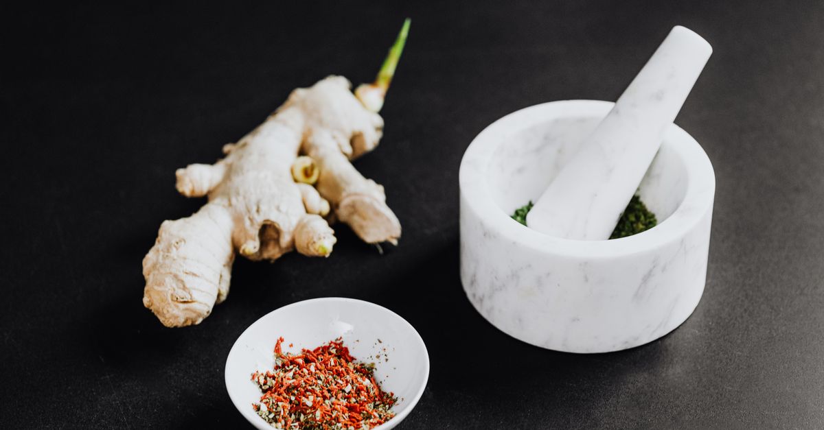 A culinary scene featuring a mortar with spices and ginger root on a black background.