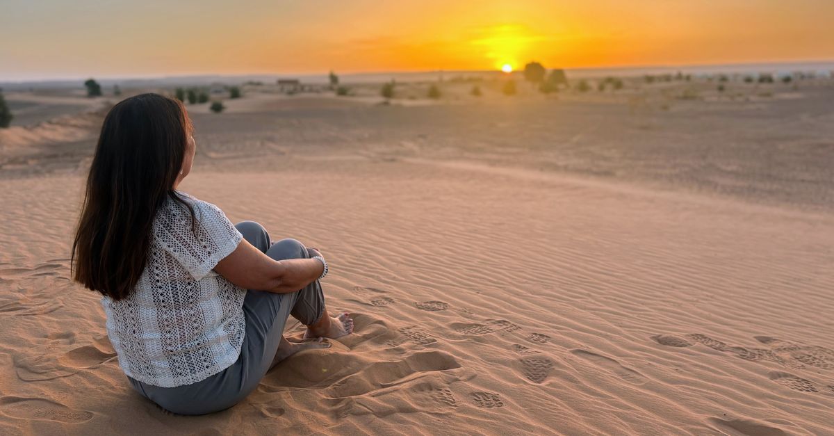 A woman enjoying the serene desert sunset, sitting on sand dunes for a moment of peace.