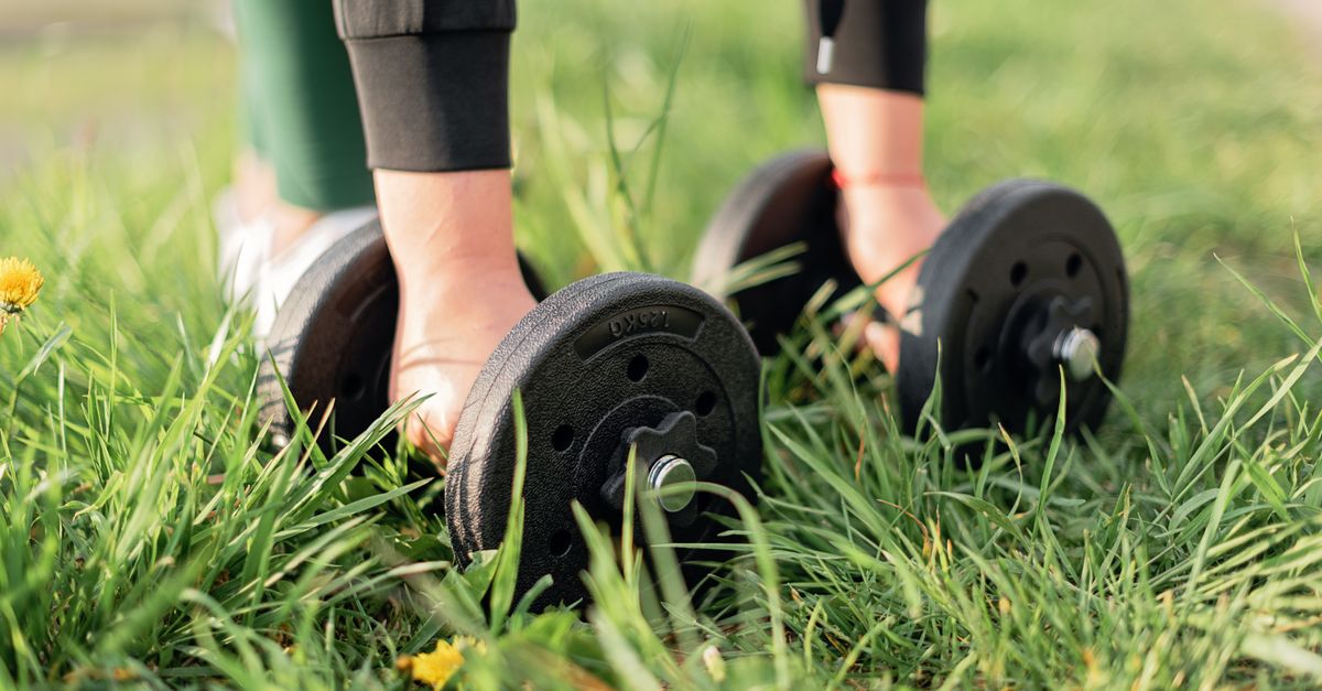 Close-up of a person exercising outdoors with dumbbells on grass, emphasizing fitness and wellness.