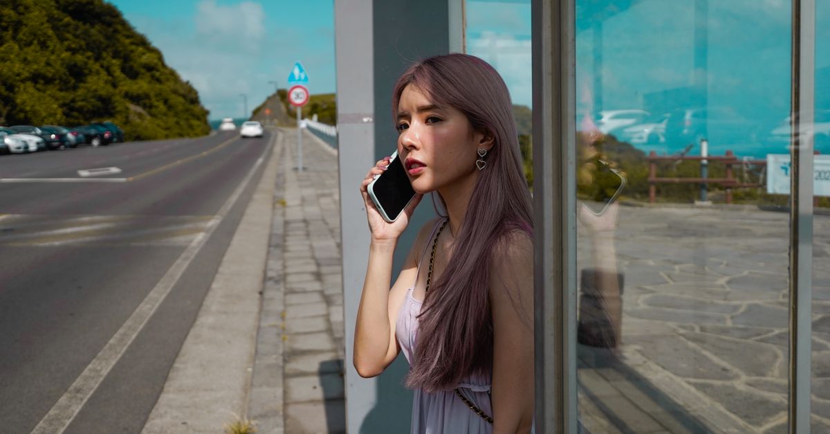 Stylish woman with dyed hair using a smartphone at a roadside, outdoors setting.