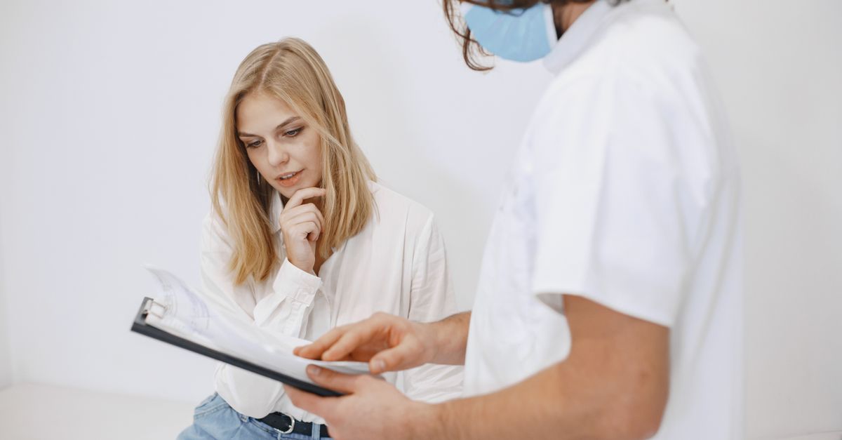 A doctor in a face mask discusses diagnosis with a patient in a clinic setting.