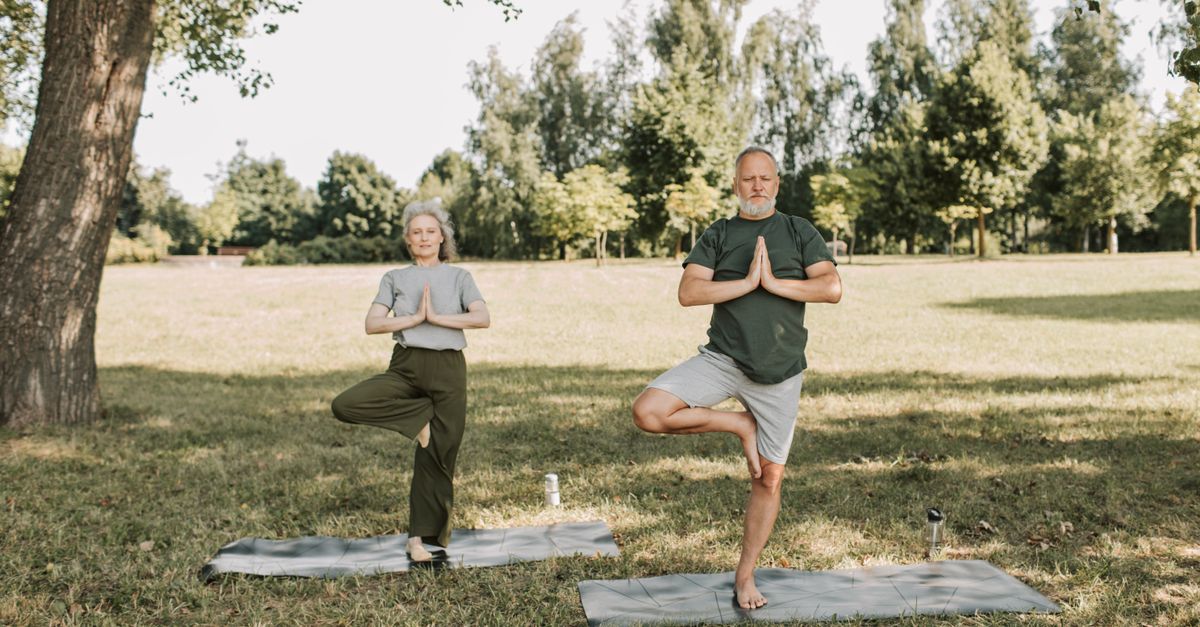 An elderly couple doing yoga in a serene park setting, promoting a healthy lifestyle.